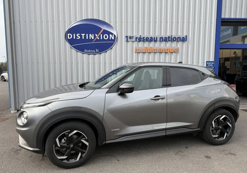 Vue de profil côté gauche du Nissan Juke 1.6 HEV gris squale métal avec jantes noires et détails hybrides visibles.