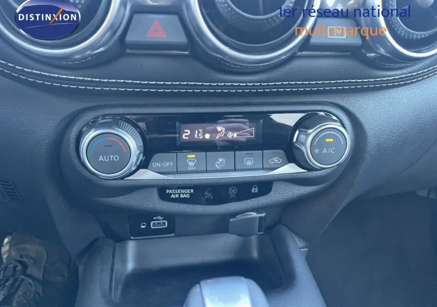 Gros plan sur la console centrale du Nissan Juke gris, montrant les commandes de climatisation automatique et la prise USB.