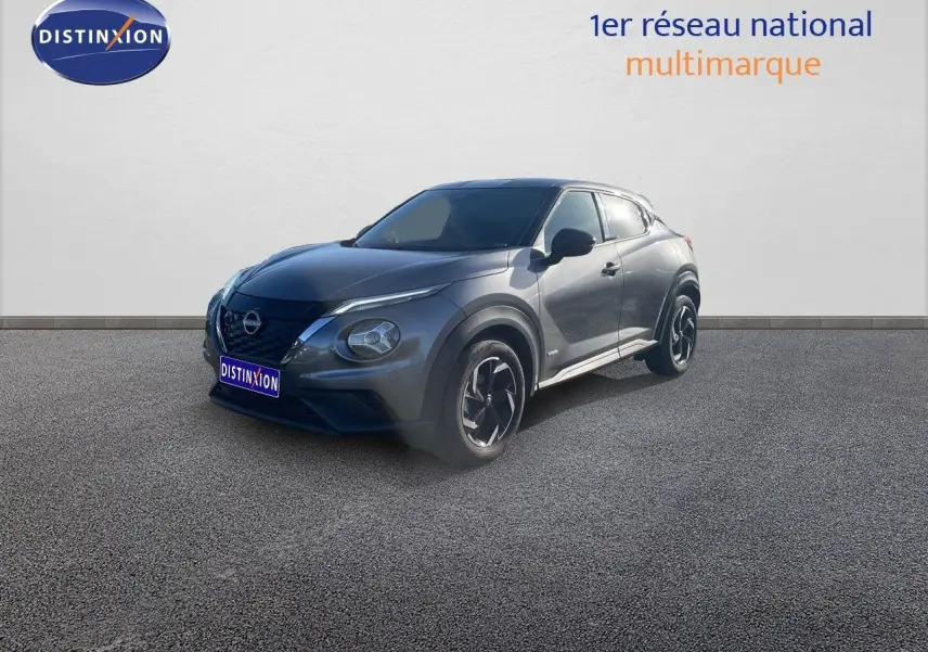 Nissan Juke 2024 gris squale métal en 3/4 avant droit, avec jantes biton et calandre noire distinctive.