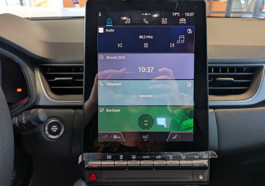 Écran tactile central du tableau de bord Renault Captur 2025 avec commandes climatisation et bouton start/stop visible.