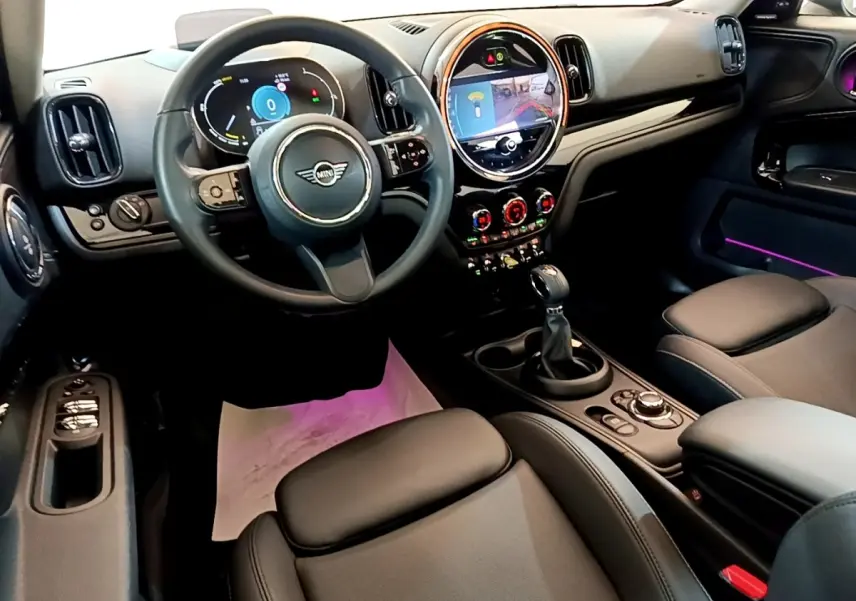 Intérieur avant droit du MINI Countryman vert 2023, volant cuir, écran tactile rond et éclairage d’ambiance violet.