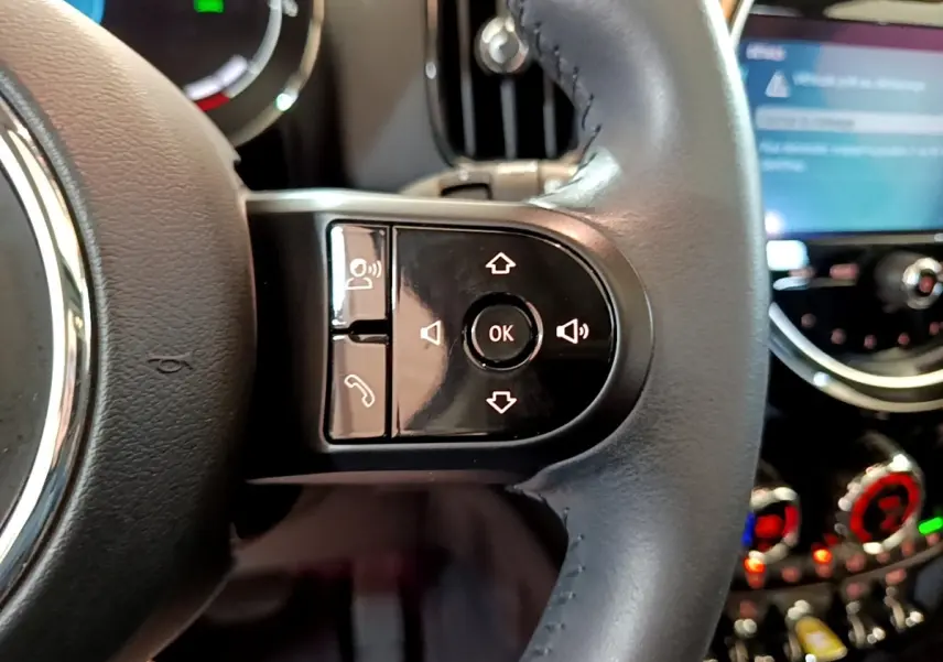 Gros plan sur les commandes du volant cuir noir du MINI COUNTRYMAN 2023, avec écran tactile flou en arrière-plan.