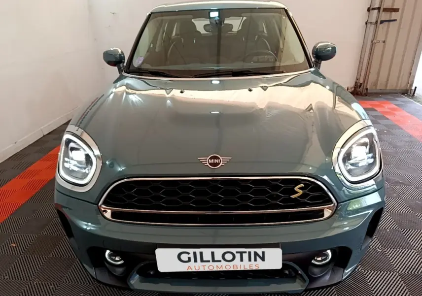 Vue avant d'une MINI Countryman Cooper SE hybride rechargeable vert avec phares LED et calandre noire en intérieur showroom.