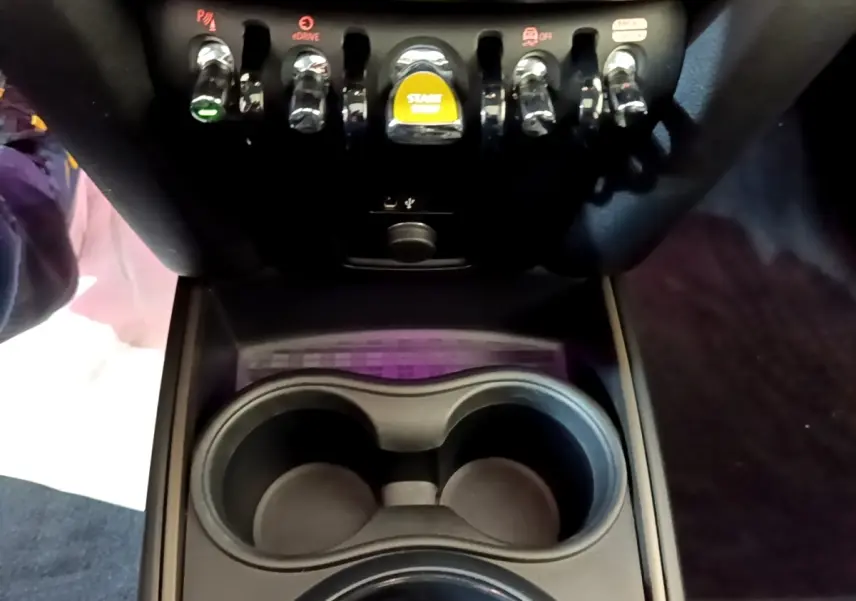 Gros plan sur la console centrale noire du MINI Countryman 2023 avec boutons de commande et bouton start/stop jaune.