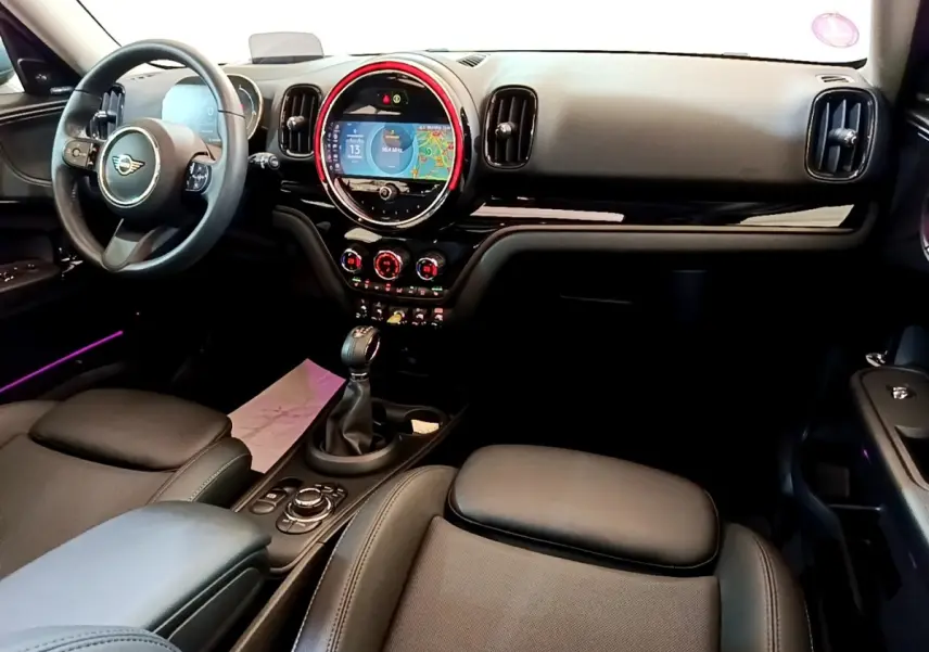 Intérieur avant du MINI Countryman Cooper SE 2023, tableau de bord noir avec écran tactile circulaire et éclairage d'ambiance rouge.