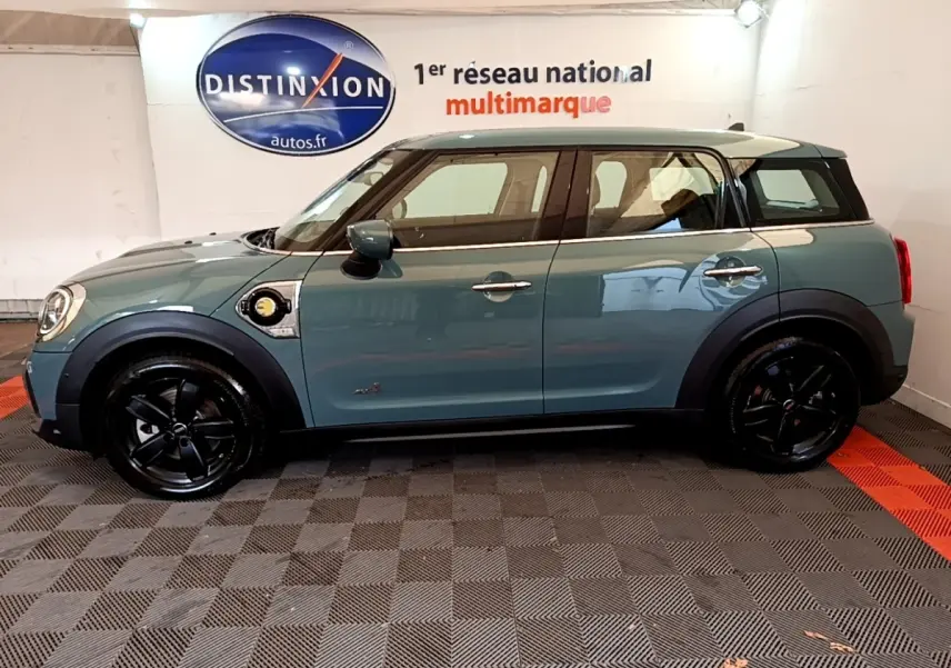 Profil côté gauche d'une MINI Countryman Cooper SE hybride rechargeable verte avec toit blanc et jantes noires.