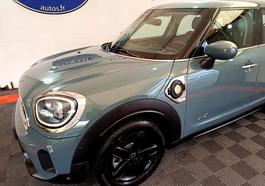 Vue 3/4 avant droit d'une MINI Countryman Cooper SE hybride rechargeable vert avec jantes noires et prise de charge latérale visible.