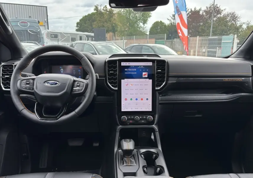 Vue intérieure frontale du Ford Ranger Wildtrak Plus 2025 noir agate, avec grand écran tactile vertical et volant cuir multifonctions.
