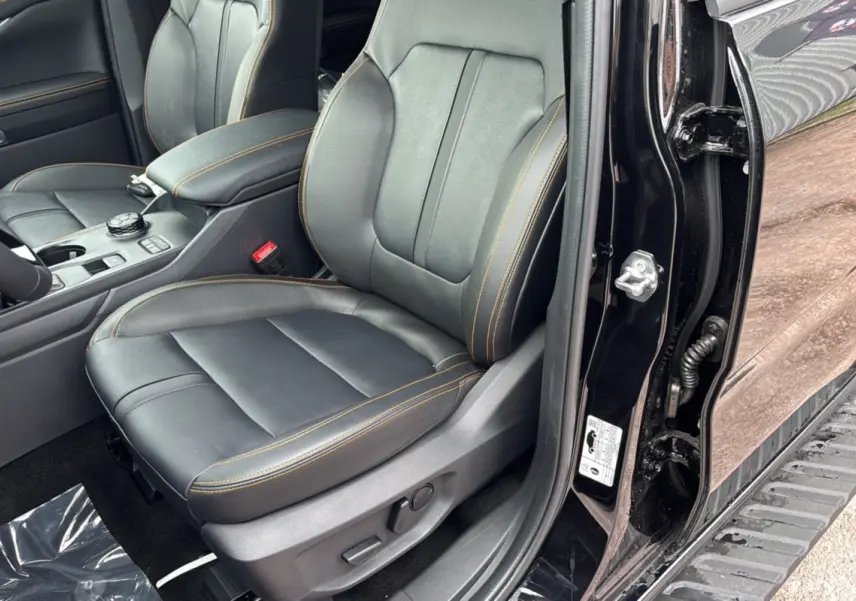 Vue intérieure côté conducteur du Ford Ranger noir agate 2025, siège en cuir noir avec surpiqûres orange et accoudoir central.