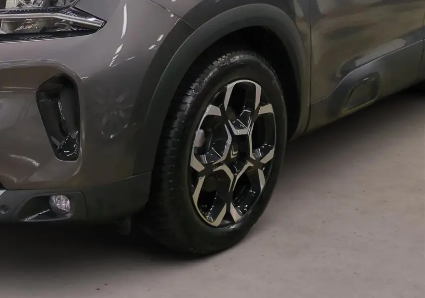 Gros plan sur la roue avant droite et l'aile d'un Citroën C5 Aircross gris Platinium avec jante alliage bi-ton.