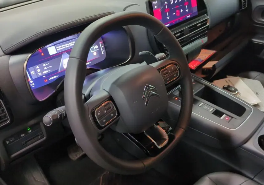 Vue intérieure centrée sur le volant cuir noir et le tableau de bord numérique du Citroën C5 Aircross Hybrid 2025.