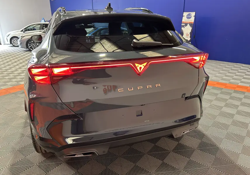 Vue arrière du CUPRA Formentor bleu Fjord métal avec feux LED allumés et hayon électrique visible en intérieur showroom.