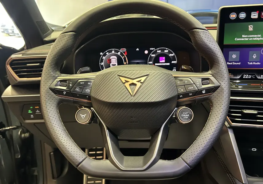 Vue rapprochée du volant en cuir perforé avec logo Cupra doré, tableau de bord numérique et écran tactile du Formentor.