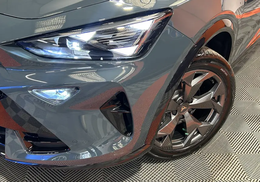 Gros plan sur l'avant droit bleu fjord métallisé du CUPRA Formentor 1.5 eTSI avec phare LED et jante alliage distinctive.
