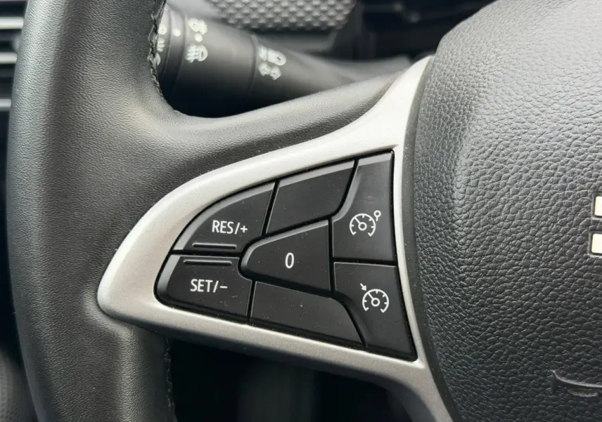 Gros plan sur les commandes du régulateur de vitesse au volant noir du Dacia Jogger Vert Cèdre métallisé.