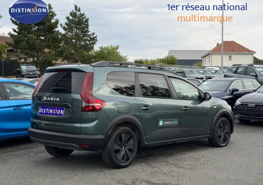 Vue 3/4 arrière droite d'un Dacia Jogger 2025 vert cèdre métallisé avec barres de toit et vitres teintées.