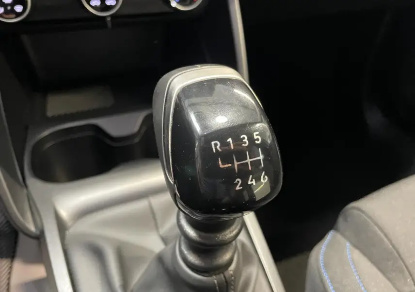 Gros plan sur le levier de vitesses manuel noir dans l’habitacle sombre de la Citroën C3 blanche.