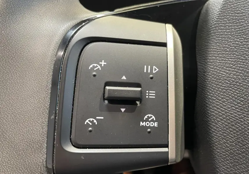 Gros plan sur les commandes de régulateur de vitesse à gauche du volant dans l’habitacle d’une Citroën C3 blanche.