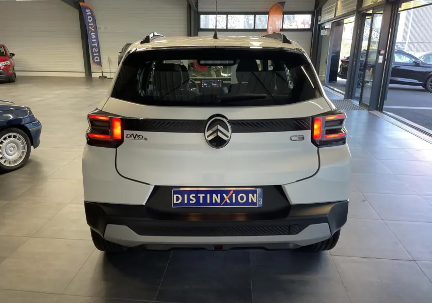 Vue arrière d'une Citroën C3 blanche 2025 avec feux LED et barres de toit noir brillant en showroom.