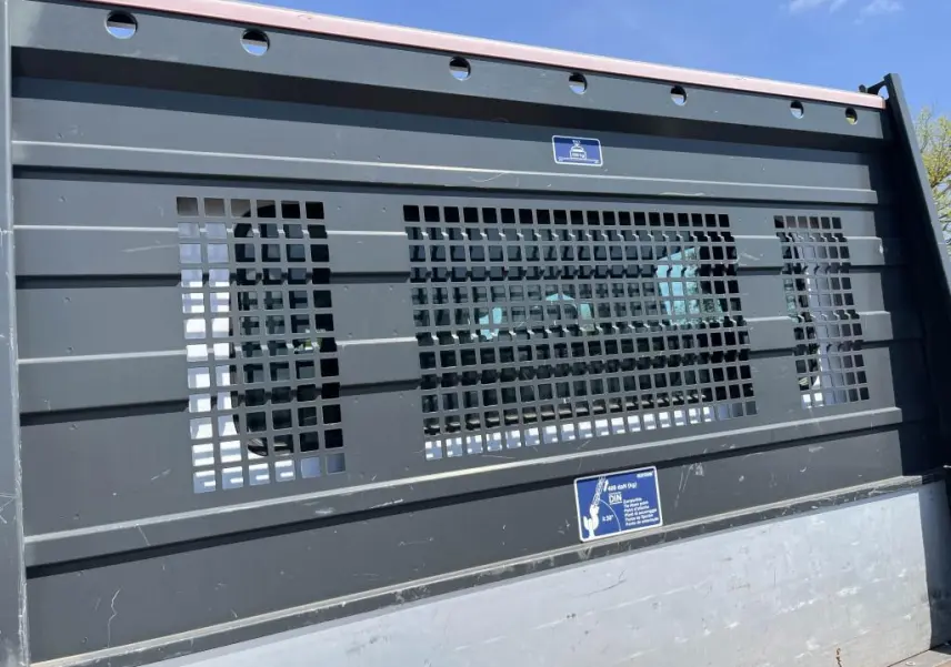 Gros plan sur la grille noire du plateau ridelles aluminium du Renault Master blanc, vue arrière sous ciel bleu.