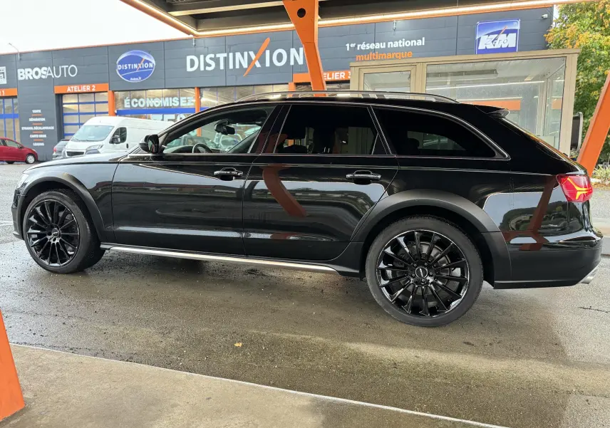 Audi A6 Avant Allroad noire vue de profil côté gauche, avec jantes noires et détails de carrosserie spécifiques.