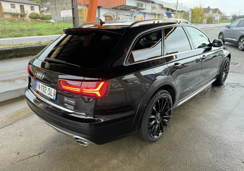 Audi A6 Avant Allroad noire vue 3/4 arrière droit, avec jantes noires et feux arrière LED allumés.