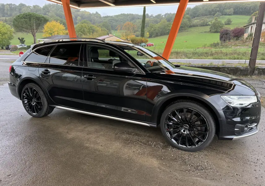 Audi A6 Avant Allroad noire vue de profil côté gauche, avec jantes noires et toit ouvrant sous abri.
