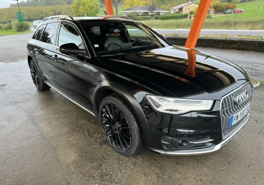 Audi A6 Avant Allroad noire vue en 3/4 avant droit, avec jantes noires et calandre chromée sous abri.