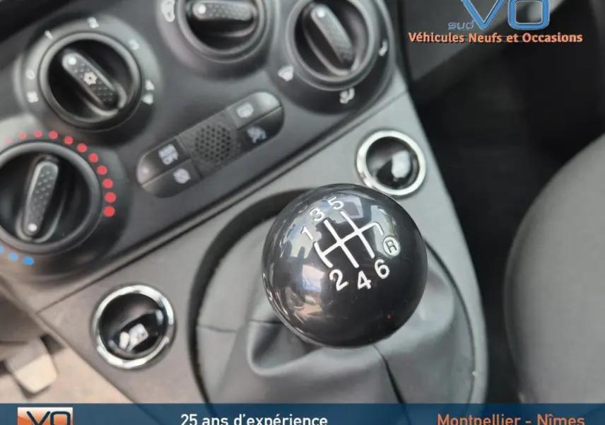 Gros plan sur le levier de vitesses manuel noir de la FIAT 500C 2024, avec commandes de climatisation en arrière-plan.