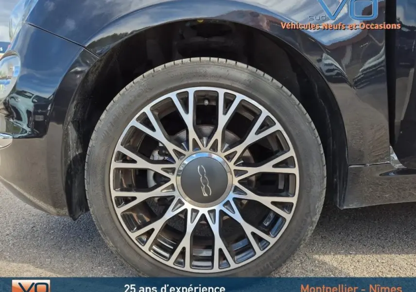 Gros plan sur la roue avant gauche noire d'une FIAT 500C 2024 avec jante alliage et roue de secours visible.