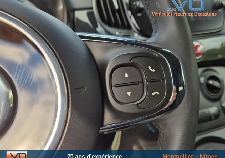 Gros plan sur les commandes du volant noir de la FIAT 500C 2024 hybride essence avec boîte manuelle.