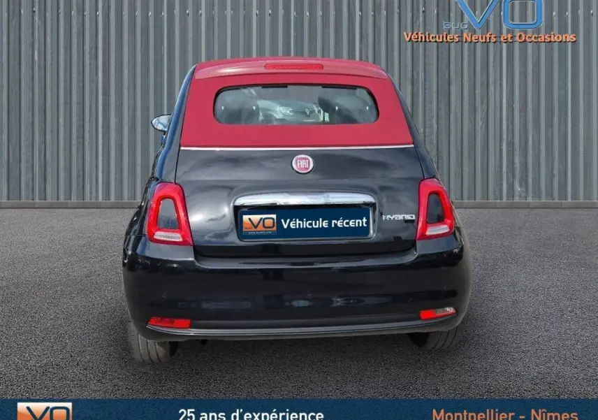 Vue arrière d'une FIAT 500C noire 2024 avec toit rouge et badge hybride, stationnée sur sol gris uniforme.