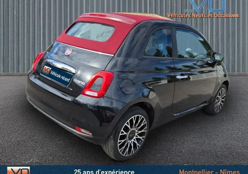 Vue 3/4 arrière droite d'une FIAT 500C noire 2024 avec toit rouge et jantes alliage, version hybride essence avec roue de secours.