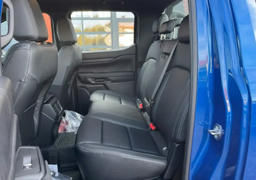 Vue côté droit de l'intérieur arrière du Ford Ranger 2025 bleu lightning avec sièges en cuir noir et ceintures de sécurité visibles.