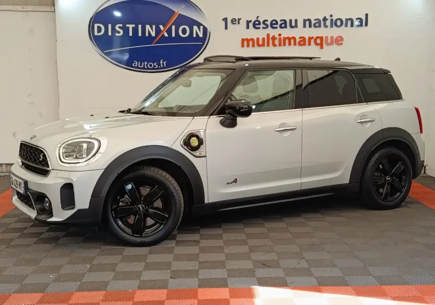 Vue latérale gauche d'un MINI Countryman Cooper SE blanc avec toit noir et jantes noires en intérieur showroom.
