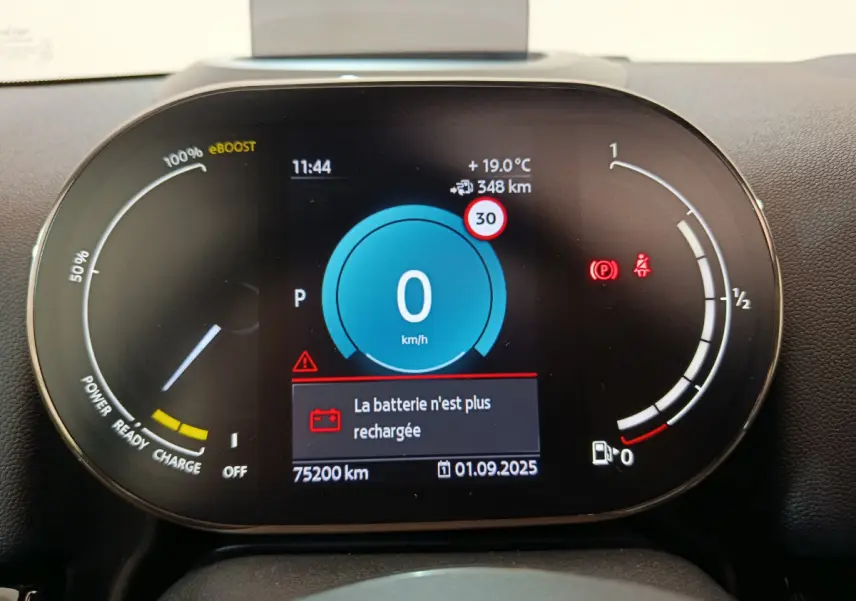 Tableau de bord numérique du MINI Countryman hybride, affichant vitesse zéro et alerte batterie déchargée.