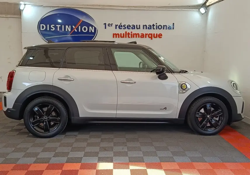 Profil droit d'un MINI COUNTRYMAN Cooper SE blanc avec toit noir et jantes noires dans un showroom.