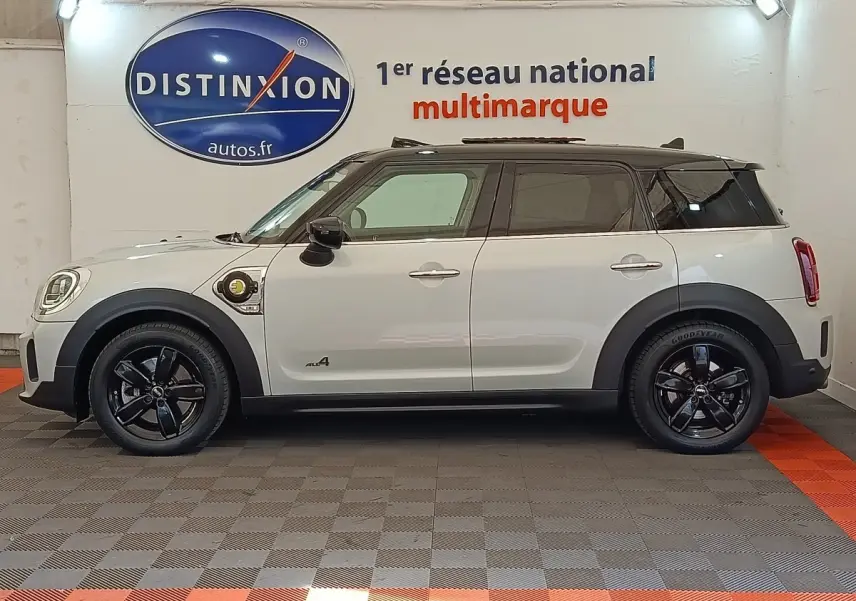 Profil côté gauche d'un MINI Countryman Cooper SE blanc avec jantes noires et prise de recharge visible sur l'aile avant.
