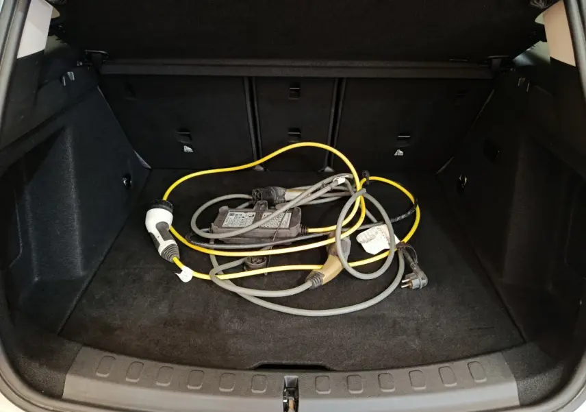 Coffre ouvert d'une MINI Countryman blanc, vue de l'arrière montrant un câble de recharge hybride posé au sol.