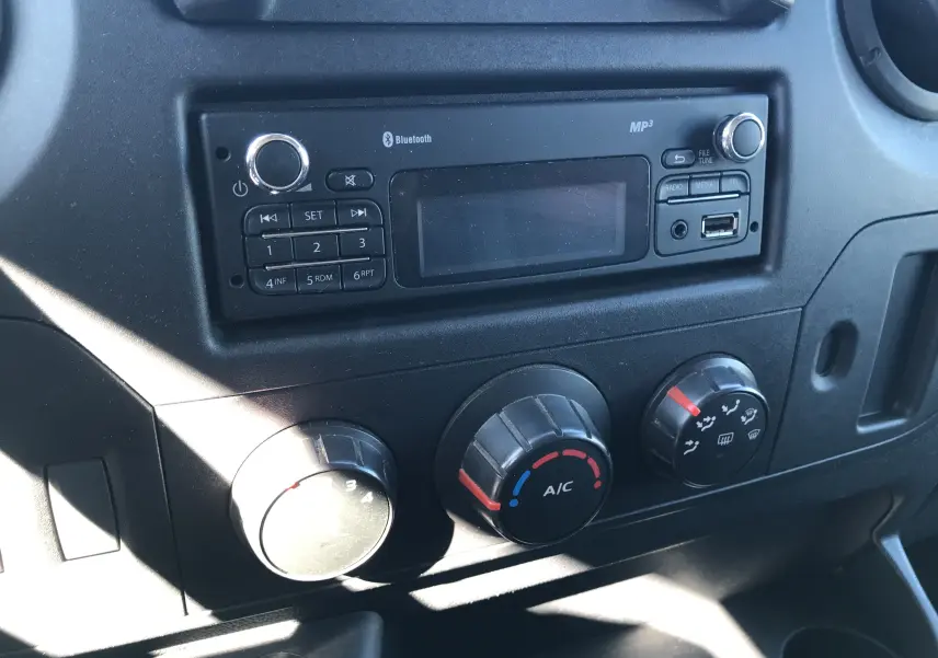 Gros plan sur la console centrale noire du Renault Master 2016, mettant en valeur la radio Bluetooth et les commandes de climatisation.