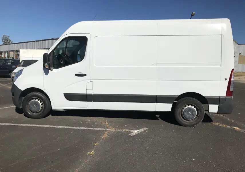 Vue latérale côté gauche d’un utilitaire Renault Master blanc avec bande noire sur le bas de caisse, stationné en extérieur.