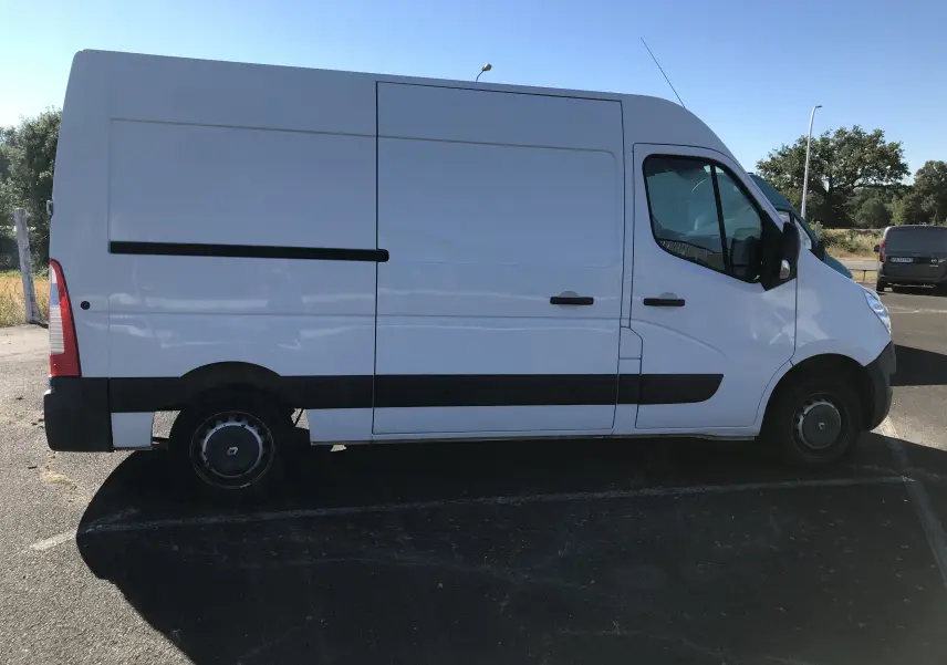 Profil droit d'un utilitaire Renault Master blanc 2016 avec porte coulissante et jantes tôles noires.