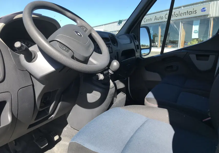 Vue intérieure côté conducteur du Renault Master blanc 2016, volant, tableau de bord et sièges en tissu bleu visibles.