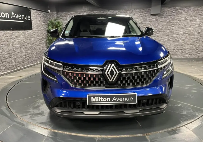 Vue frontale du Renault Austral bleu avec calandre à damier chrome sombre et logo Renault central lumineux.