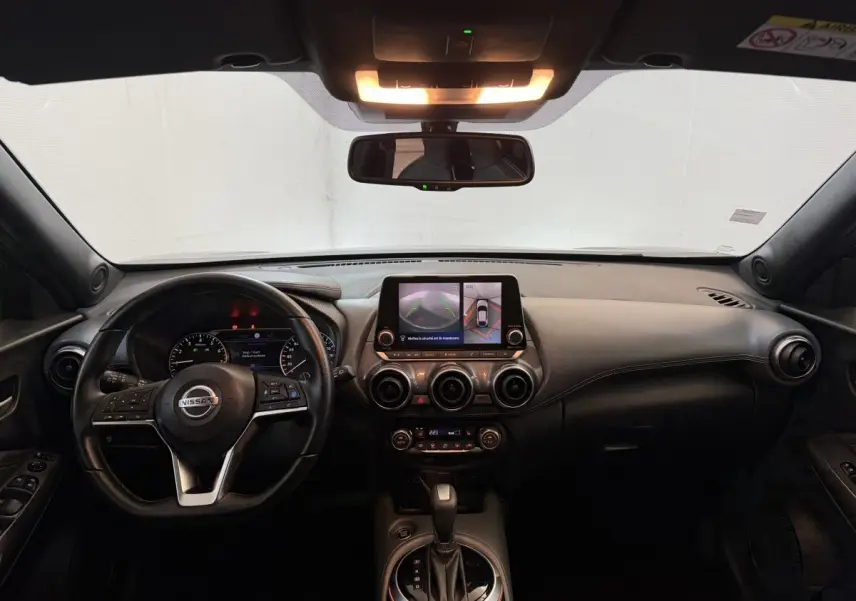 Vue intérieure avant du Nissan Juke gris clair 2021, tableau de bord avec écran tactile et volant cuir multifonctions.