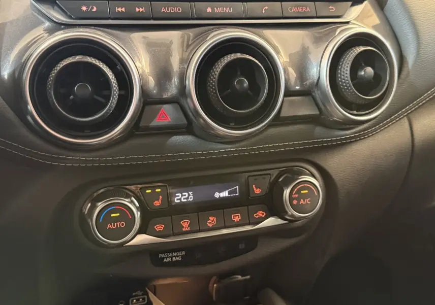 Détail du tableau de bord du Nissan Juke Tekna 2021 montrant les commandes de climatisation et les aérateurs ronds noirs.