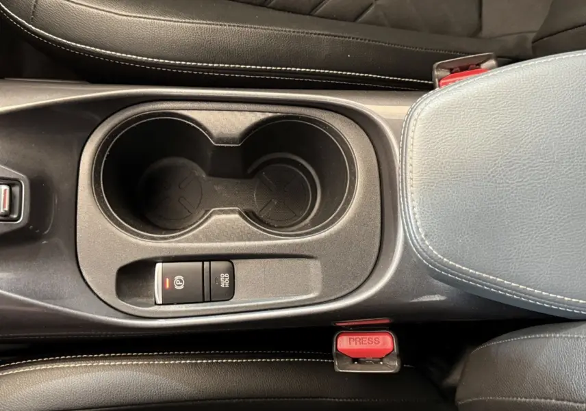 Gros plan sur la console centrale noire du Nissan Juke gris clair, avec porte-gobelets et frein à main électrique.