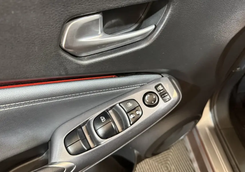 Gros plan sur la porte côté conducteur du Nissan Juke gris clair, montrant les commandes électriques et la poignée intérieure argentée.