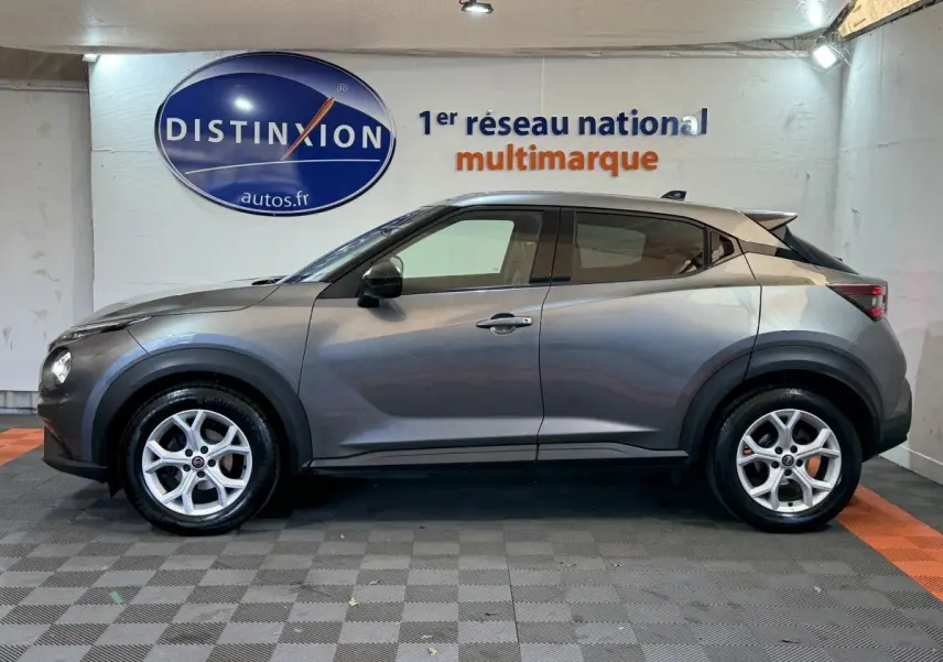 Profil côté gauche d'un Nissan Juke gris clair 2021 avec jantes argentées, dans un showroom intérieur.