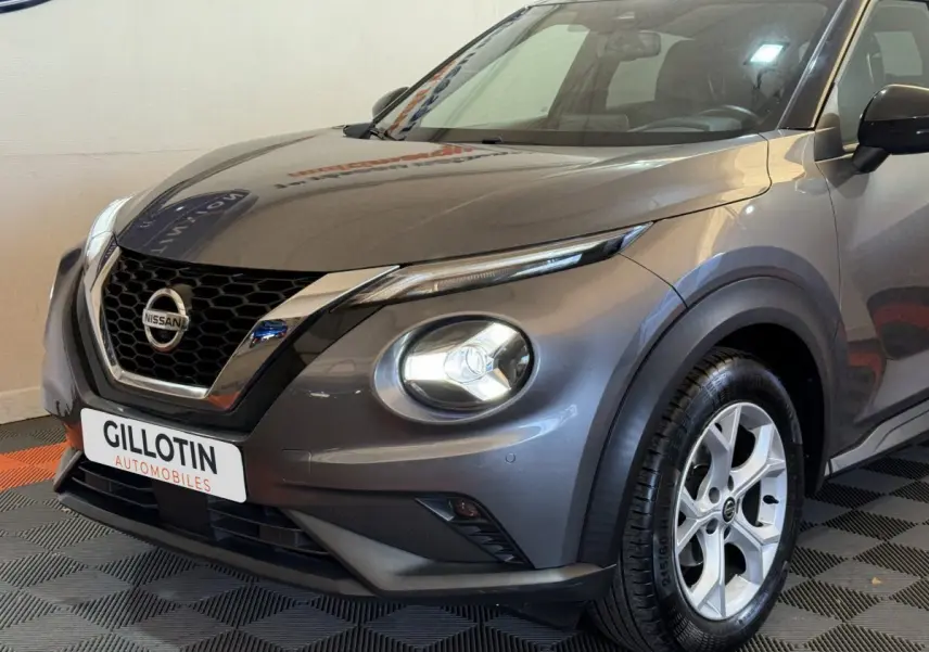 Vue 3/4 avant droit d'un Nissan Juke gris clair avec phares LED ronds et calandre en nid d'abeille chromée.